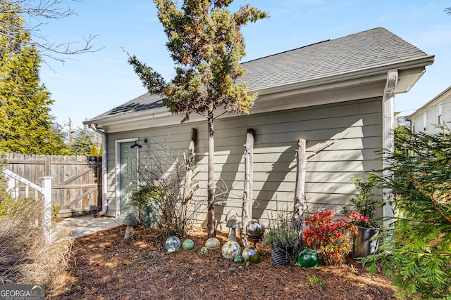 view of property exterior featuring a shingled roof and fence