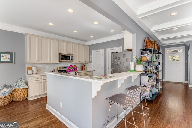 kitchen featuring dark wood-type flooring, a kitchen bar, a peninsula, cream cabinetry, and stainless steel appliances