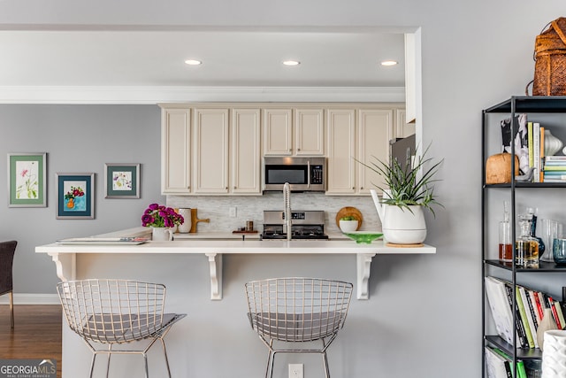 kitchen featuring stainless steel appliances, backsplash, cream cabinetry, and a breakfast bar