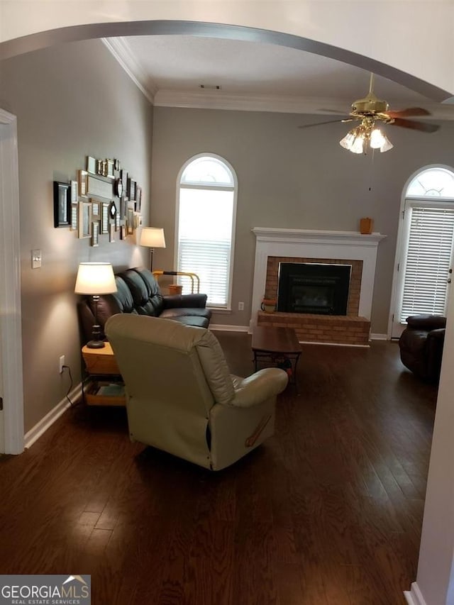 living room featuring ceiling fan, dark hardwood / wood-style floors, crown molding, and a fireplace