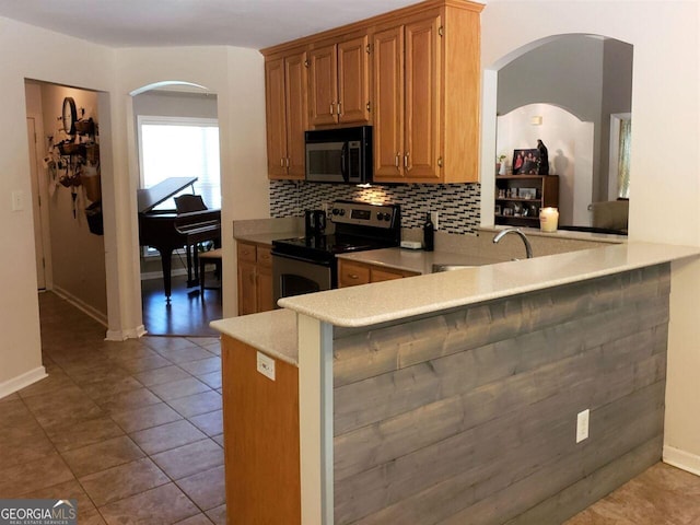 kitchen with kitchen peninsula, stainless steel electric stove, tasteful backsplash, light tile patterned floors, and a kitchen bar