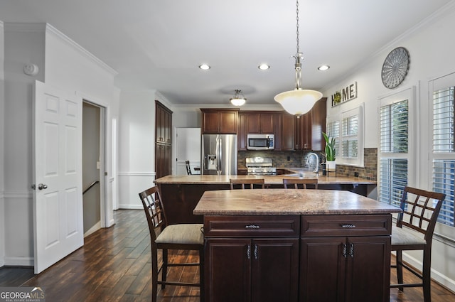 kitchen featuring dark wood-type flooring, decorative light fixtures, a center island, ornamental molding, and appliances with stainless steel finishes