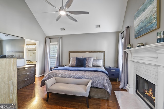 bedroom with ceiling fan, hardwood / wood-style floors, connected bathroom, a brick fireplace, and vaulted ceiling