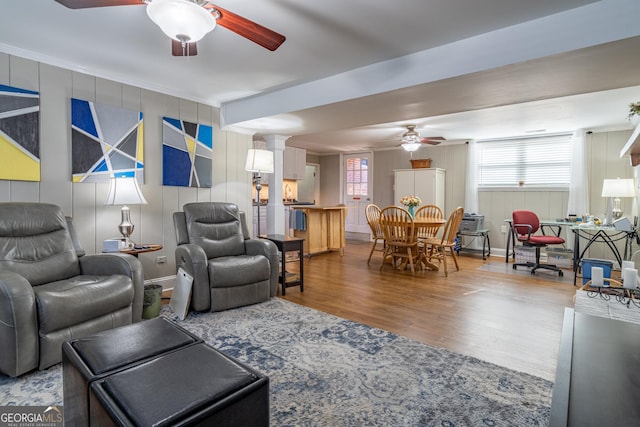 living room with wood-type flooring, decorative columns, wooden walls, and ceiling fan