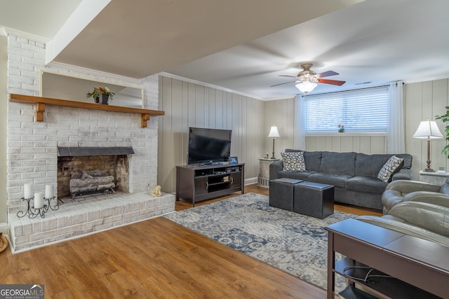 living room featuring wood-type flooring, ceiling fan, a brick fireplace, and crown molding