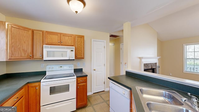 kitchen featuring sink, vaulted ceiling, a stone fireplace, and white appliances