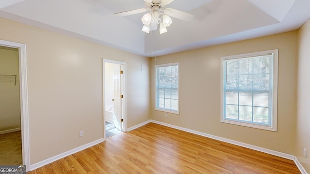 unfurnished bedroom featuring ceiling fan, a raised ceiling, ensuite bath, a walk in closet, and a closet