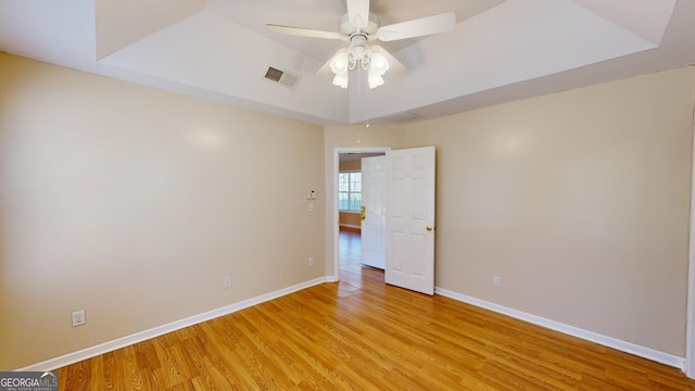 unfurnished room with light hardwood / wood-style floors, a raised ceiling, and ceiling fan