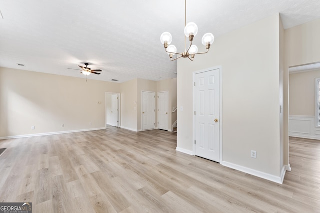 empty room with a textured ceiling, light wood-type flooring, and ceiling fan with notable chandelier