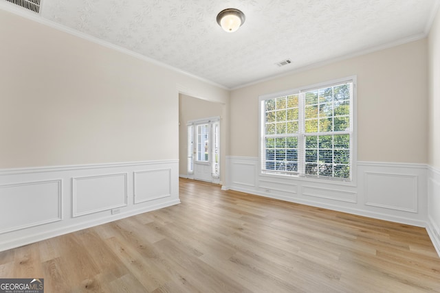 empty room with light hardwood / wood-style flooring, a textured ceiling, and crown molding