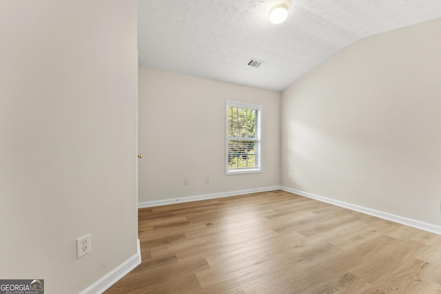 unfurnished room with a textured ceiling, lofted ceiling, and light wood-type flooring