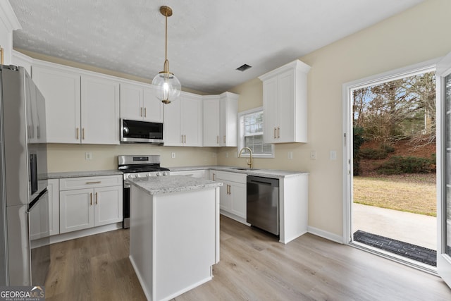 kitchen featuring stainless steel appliances, white cabinetry, a kitchen island, and decorative light fixtures