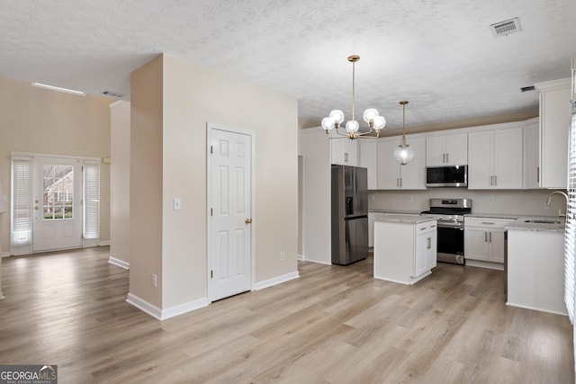 kitchen with appliances with stainless steel finishes, white cabinetry, a kitchen island, decorative light fixtures, and light stone counters