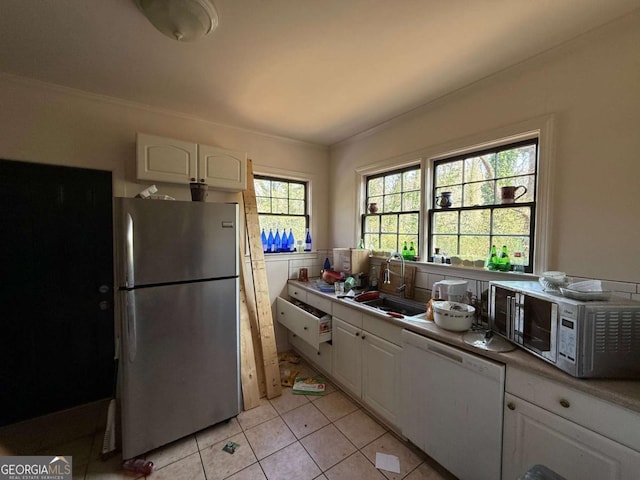 kitchen featuring dishwasher, sink, white cabinetry, light tile patterned floors, and stainless steel refrigerator