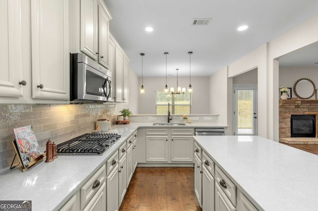 kitchen with stainless steel appliances, white cabinetry, sink, and a fireplace