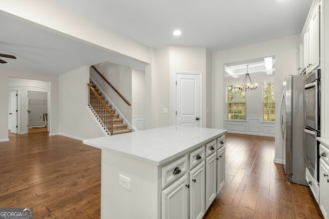 kitchen with ceiling fan with notable chandelier, white cabinetry, dark hardwood / wood-style flooring, a center island, and stainless steel appliances