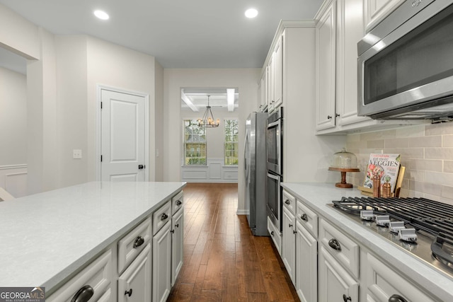 kitchen with dark wood-type flooring, backsplash, stainless steel appliances, white cabinets, and a chandelier