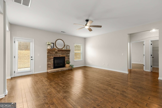 unfurnished living room featuring ceiling fan, a stone fireplace, and dark hardwood / wood-style flooring