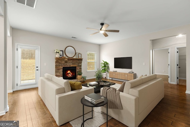 living room with ceiling fan, a stone fireplace, and hardwood / wood-style floors