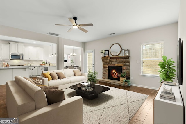 living room featuring sink, dark hardwood / wood-style flooring, ceiling fan with notable chandelier, and a stone fireplace