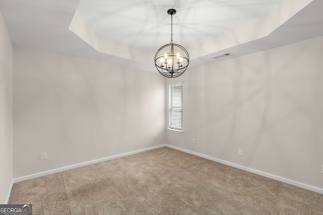 unfurnished room featuring a tray ceiling, a chandelier, and carpet flooring