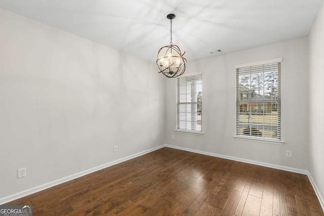 spare room featuring dark wood-type flooring and an inviting chandelier