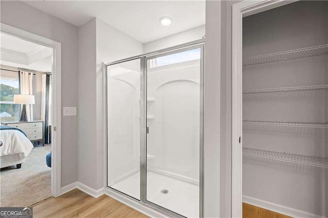 bathroom featuring wood finished floors, baseboards, a spacious closet, a stall shower, and ensuite bath