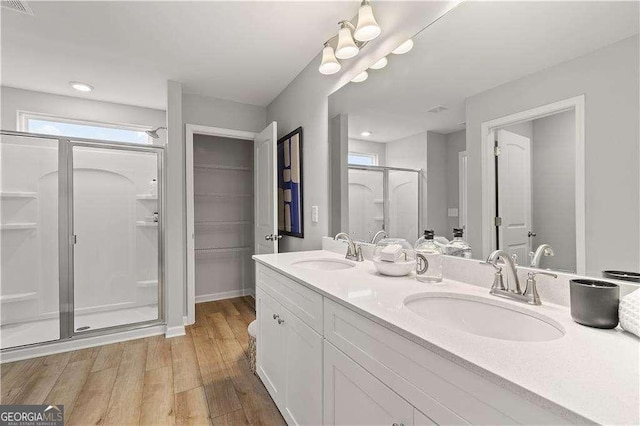 full bathroom with double vanity, a shower stall, a sink, and wood finished floors