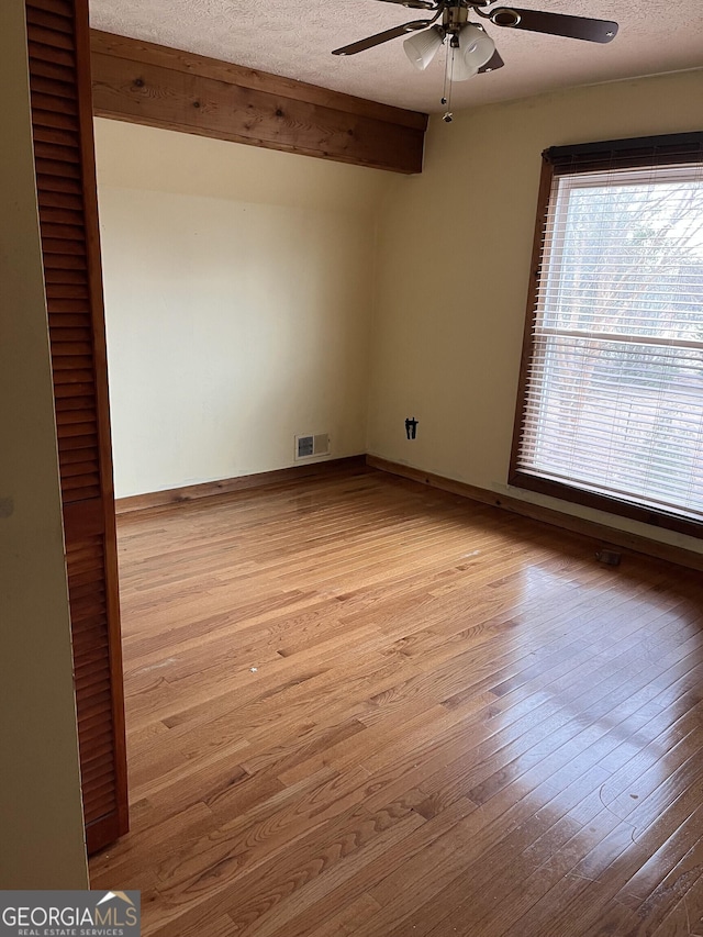 empty room with a textured ceiling, light hardwood / wood-style flooring, beamed ceiling, and ceiling fan