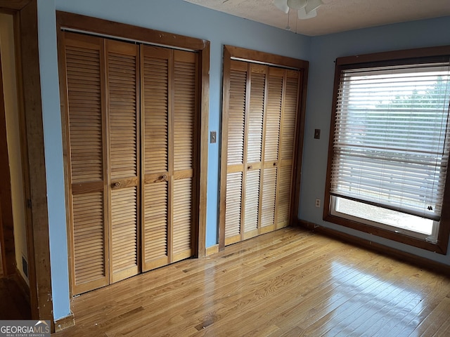 unfurnished bedroom featuring multiple closets, light wood-type flooring, a textured ceiling, and multiple windows