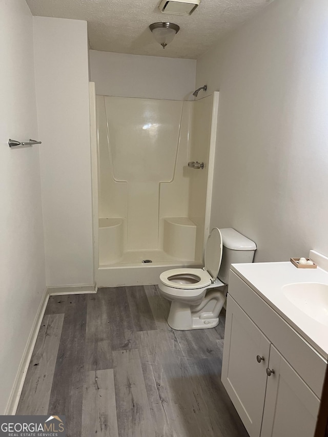 bathroom featuring wood-type flooring, a textured ceiling, toilet, and walk in shower