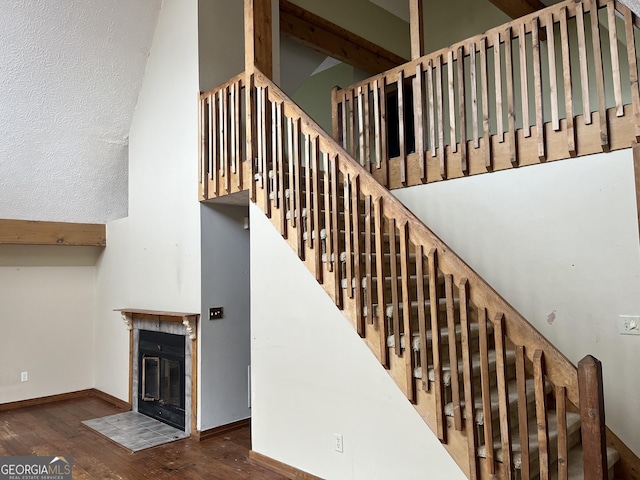 stairway with a high ceiling, wood-type flooring, and a tile fireplace