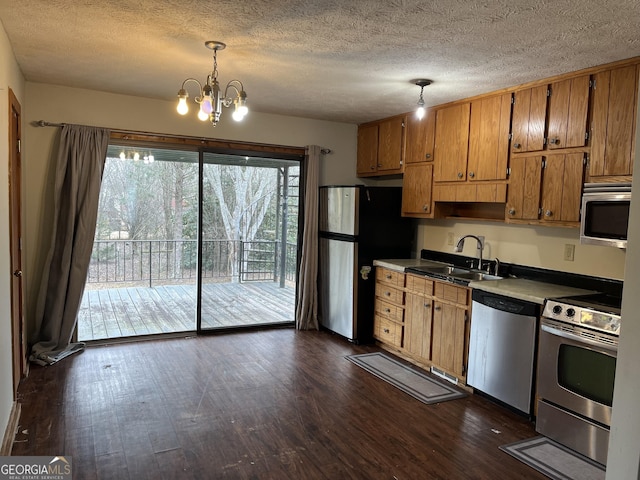 kitchen with appliances with stainless steel finishes, a textured ceiling, sink, pendant lighting, and dark hardwood / wood-style floors