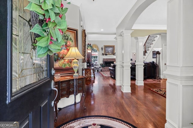 entrance foyer with dark wood-type flooring, a fireplace, crown molding, and ornate columns