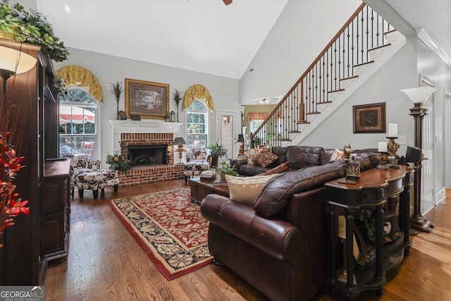 living room with high vaulted ceiling, a fireplace, hardwood / wood-style flooring, ornamental molding, and ceiling fan