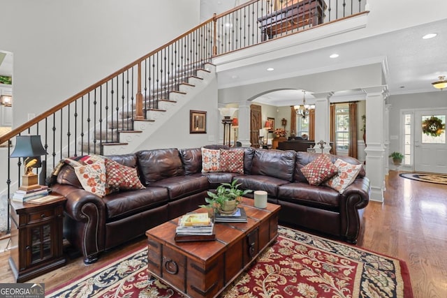 living room featuring hardwood / wood-style flooring, a high ceiling, ornamental molding, a chandelier, and ornate columns