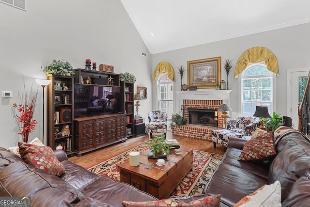 living room with hardwood / wood-style flooring, crown molding, high vaulted ceiling, and a brick fireplace