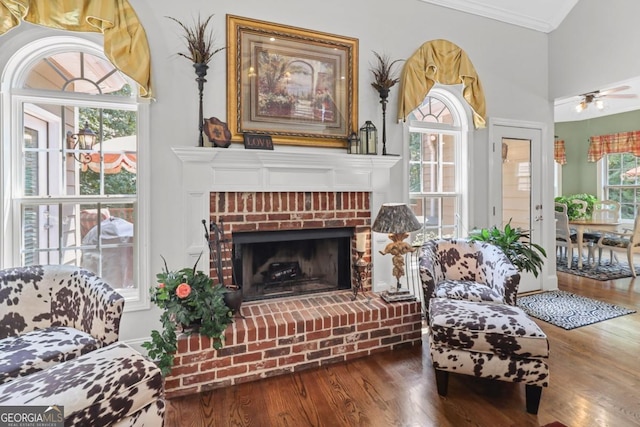 sitting room with hardwood / wood-style flooring, ceiling fan, crown molding, and a brick fireplace