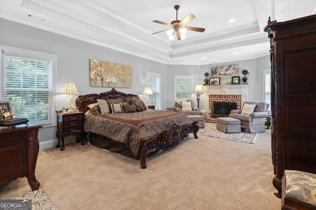 carpeted bedroom with crown molding, ceiling fan, a raised ceiling, and a brick fireplace