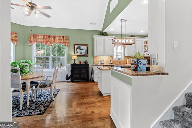 kitchen with white cabinetry, dark stone countertops, kitchen peninsula, pendant lighting, and decorative backsplash