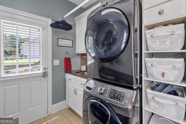 clothes washing area featuring stacked washer and dryer, light tile patterned floors, and cabinets