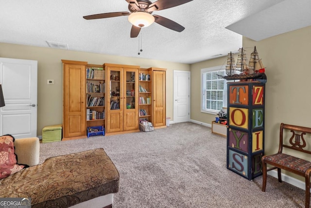 sitting room with ceiling fan, light colored carpet, and a textured ceiling