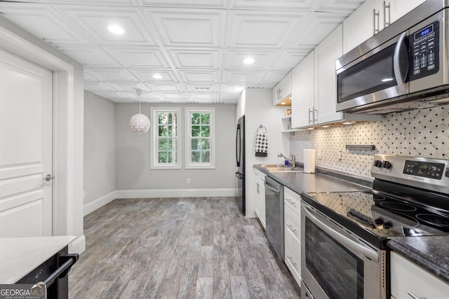 kitchen with pendant lighting, tasteful backsplash, white cabinetry, sink, and stainless steel appliances