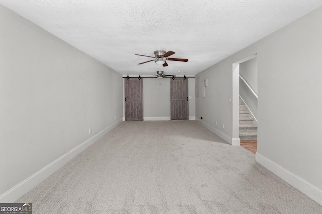 empty room with ceiling fan, a barn door, carpet floors, and a textured ceiling