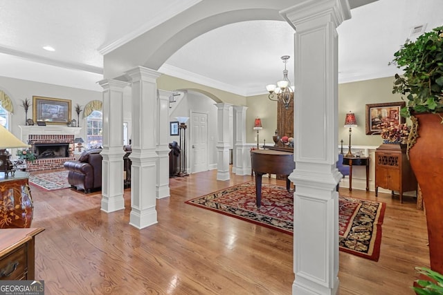 foyer with ornamental molding, a fireplace, decorative columns, and light hardwood / wood-style flooring