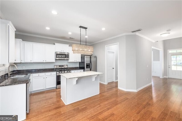 kitchen with pendant lighting, appliances with stainless steel finishes, sink, white cabinets, and a center island