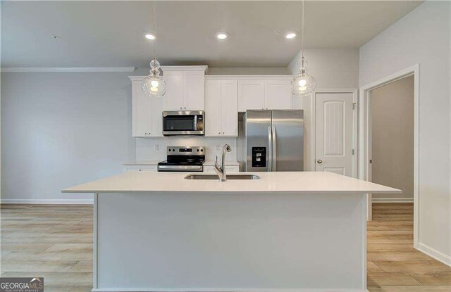 kitchen with appliances with stainless steel finishes, white cabinetry, sink, decorative light fixtures, and a center island with sink