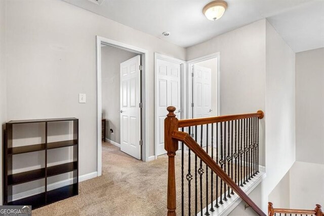 hallway featuring baseboards, light colored carpet, and an upstairs landing