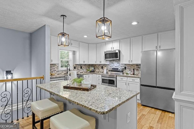 kitchen with light stone counters, light wood-style flooring, stainless steel appliances, white cabinetry, and backsplash