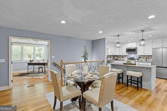 dining room with a textured ceiling, recessed lighting, light wood-type flooring, and baseboards